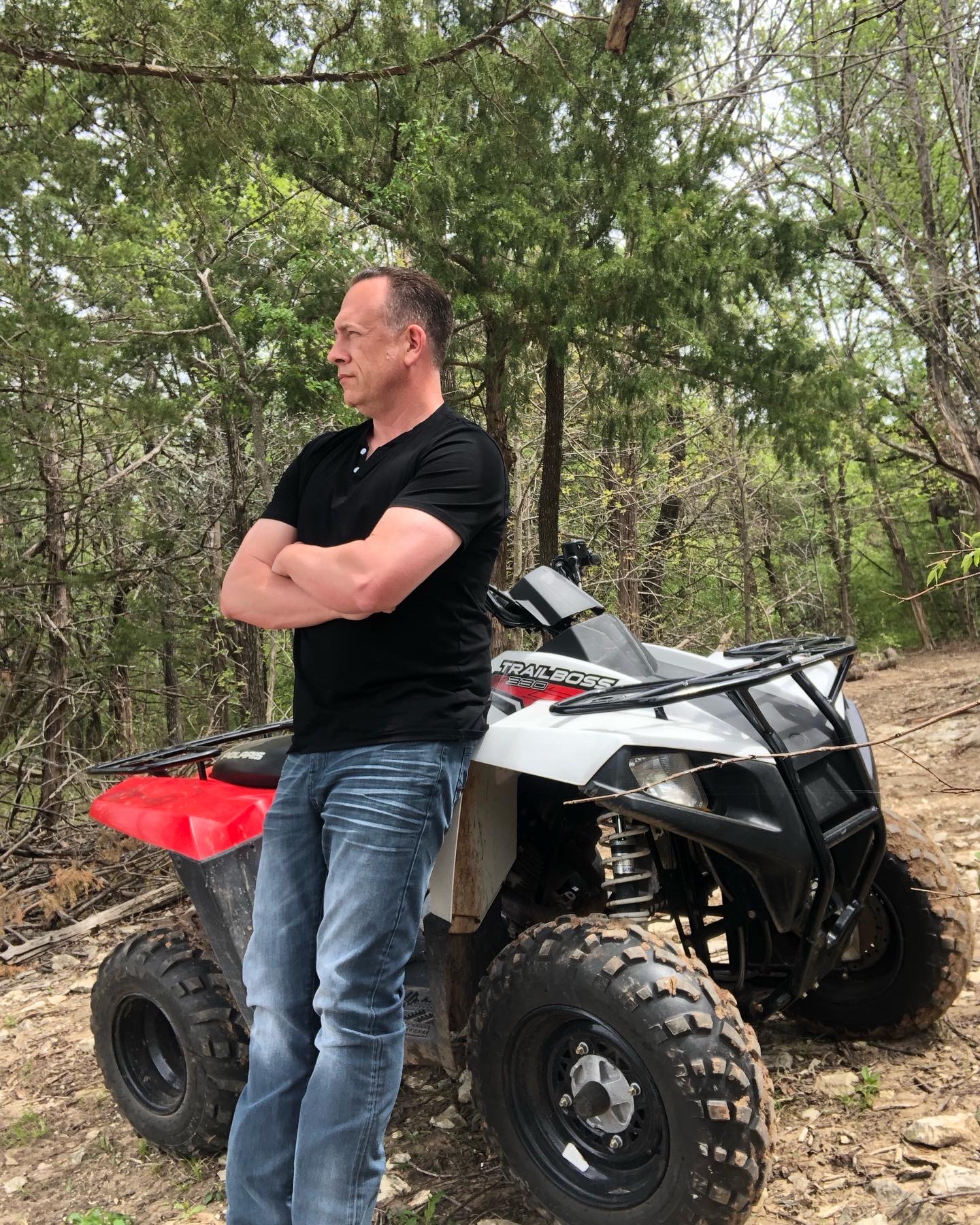Terry Larkin standing beside an ATV on a wooded trail.